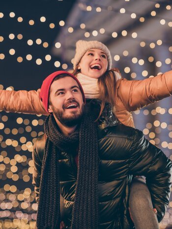Weihnachtsmarkt Reisen mit railtour | © shutterstock / 1819607177 Glückliches Pärchen  in Winterkleidung vor Weihnachtslichtern | © shutterstock / 1819607177