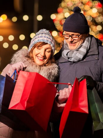Europäische Metropolen zur Weihnachtszeit zum Christmasshopping mit railtour erleben. | © shutterstock / 1494691982 Glückliches Paar mit Einkaufstaschen am Weihnachtsmarkt nach erfolgreichem Weihnachtsshopping-Tag in der festlich geschmückten Stadt
 | © shutterstock / 1494691982