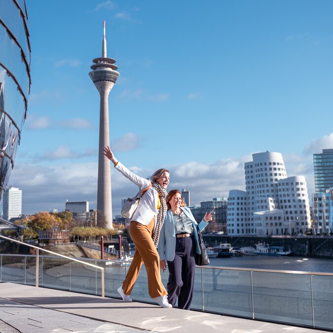 MedienHafen  | © Düsseldorf Tourismus – EU React Zwei glückliche Personen posieren für ein Foto im Medien Hafen von Düsseldorf. | © Düsseldorf Tourismus – EU React