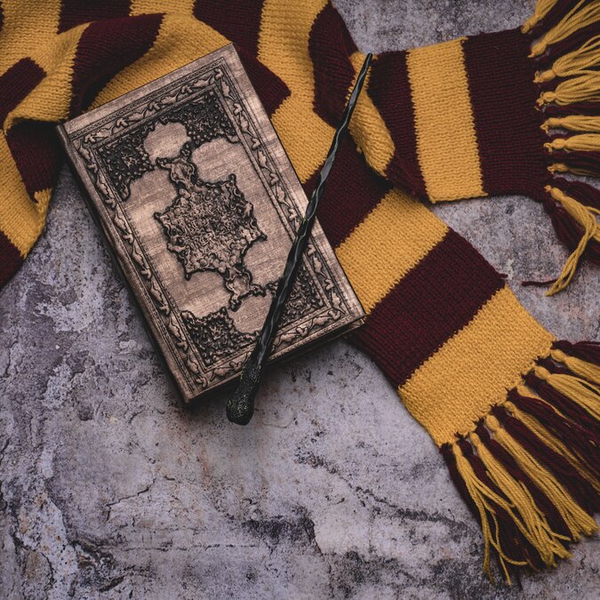 Harry Potter | © Shutterstock 1564885576 Themen der Zauberschule. Scarf, Zauberstab, Zauberbuch auf grauem Hintergrund | © Shutterstock 1564885576