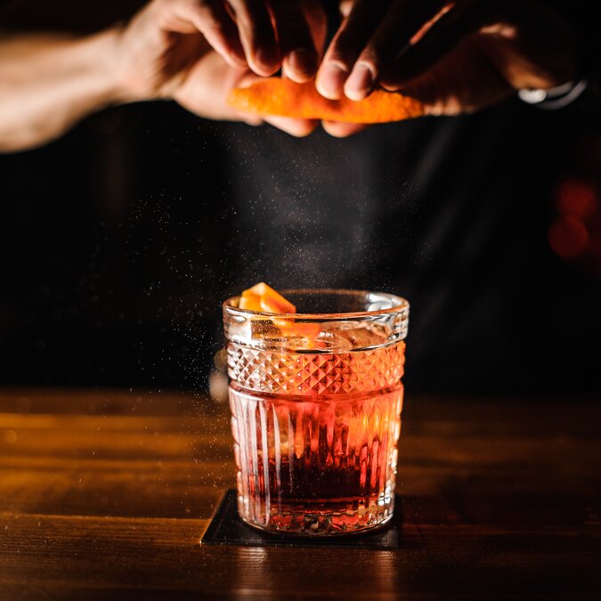 In 80 Cocktails um die Welt | © Shutterstock 711382402 Barmann mit Cocktail und Orangenschale, der Cocktail an der Bar zubereitet. | © Shutterstock 711382402