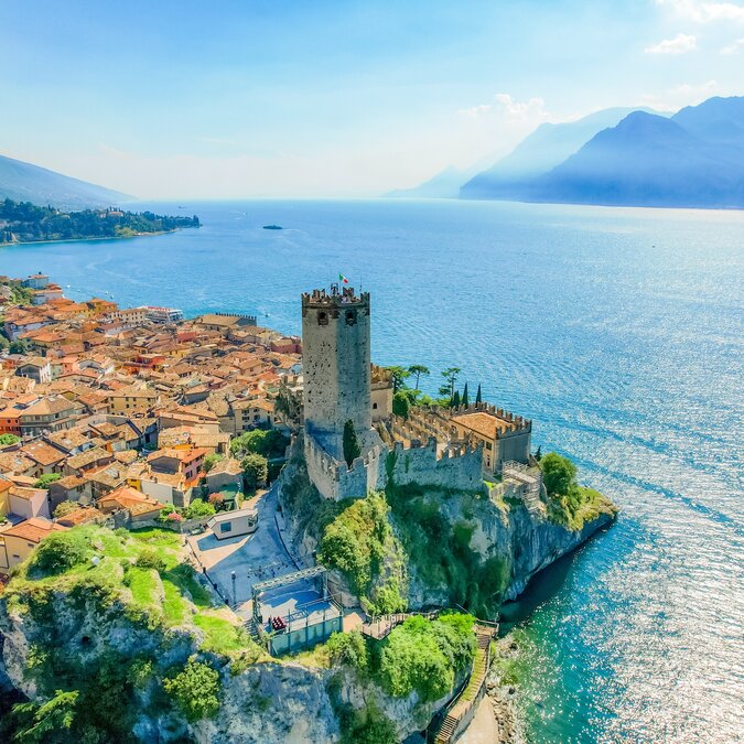 Scaligerburg in Malcesine | © shutterstock / 2498491379 Luftaufnahme vom Scalinger Castle und der Altstadt von Malcesine direkt am Ufer des Gardasees und Berge im Hintergrund | © shutterstock / 2498491379