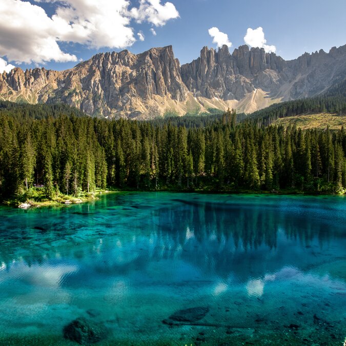 Lago di Carezza in Südtirol | © shutterstock / 2443479095 Tiefblauer See in Südtirol vor einem bewaldeten Ufer und den Dolomiten im Hintergrund | © shutterstock / 2443479095