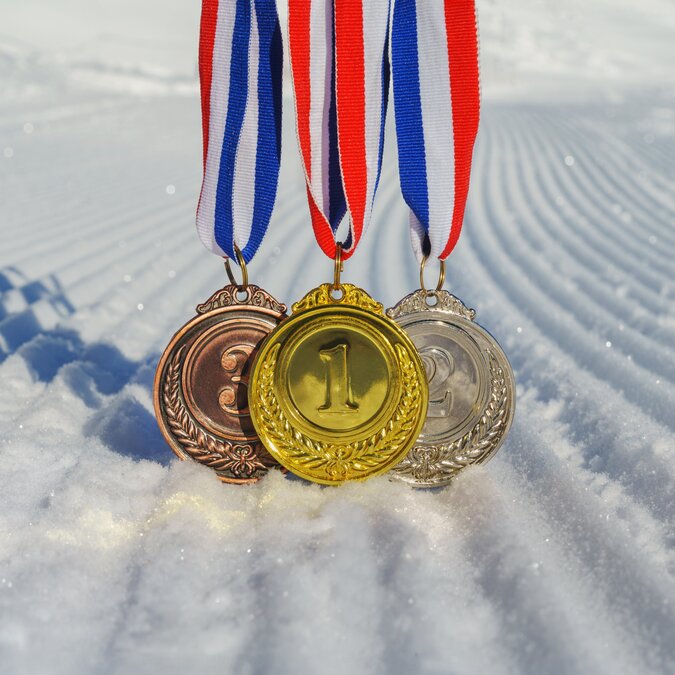 Olympische Winterspiele | © shutterstock / 2412289739 Olympische Medaillen im Schnee | © shutterstock / 2412289739